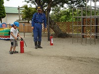 「火事だー。」先生たちと年長のお友達２人が水消化器で消火訓練をしました